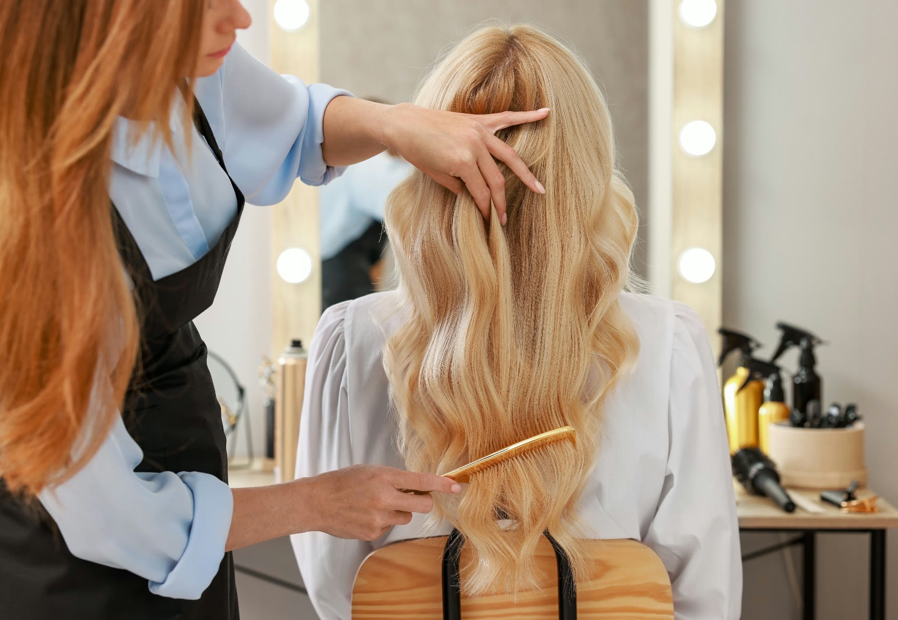 Cosmetology student combing a client's long blonde waves at a salon station